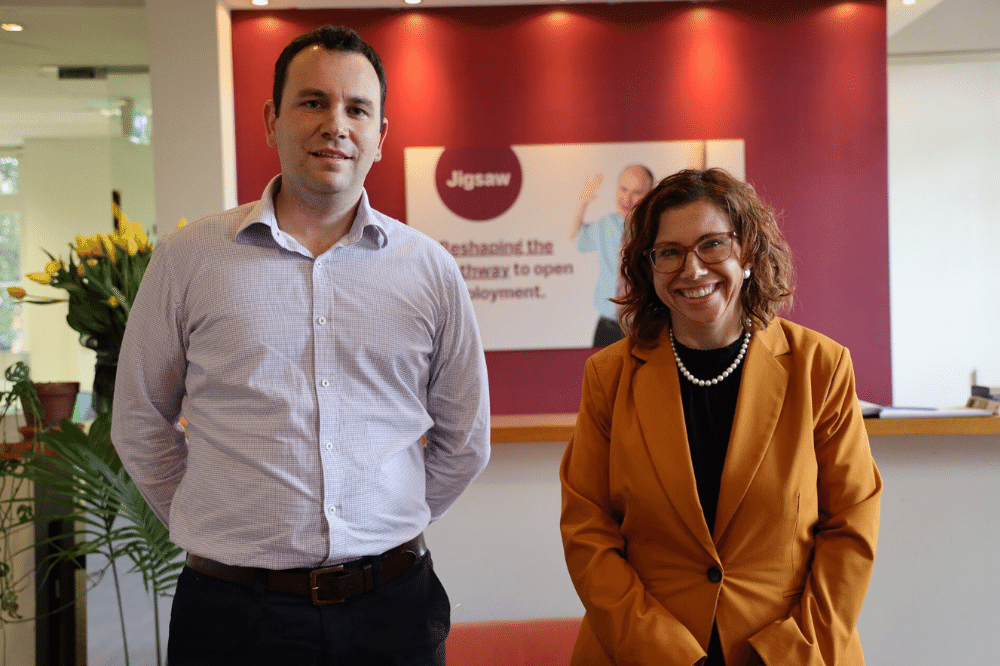 Blog tiles Minister Rishworth Paul Brown, CEO, Jigsaw wears a grey shirt. He has short dark hair. Standing next to Paul is Minister Rishworth smiling. She wears a mustard blazer and glasses.