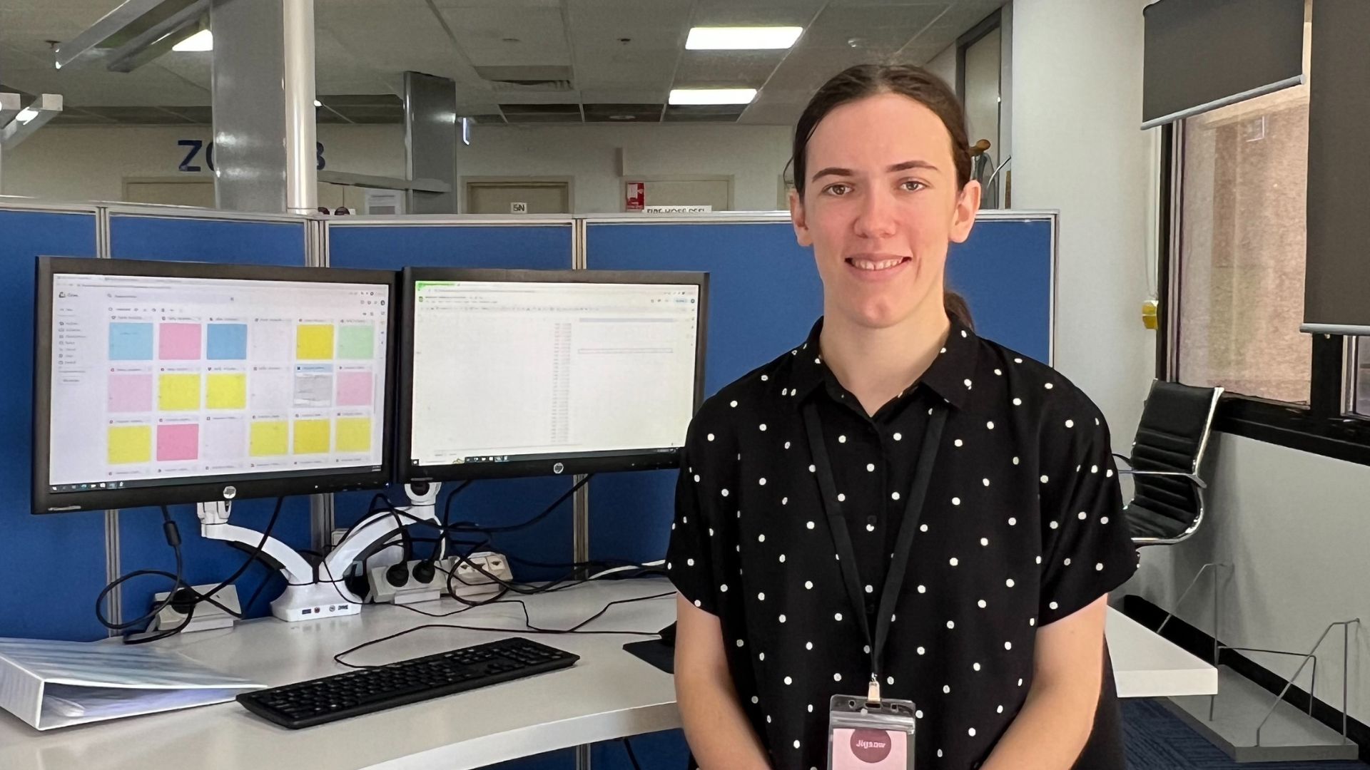 paid trainee Jayne sits in front of desk smiling at the camera. Jayne is wearing a black polka dot shirt.