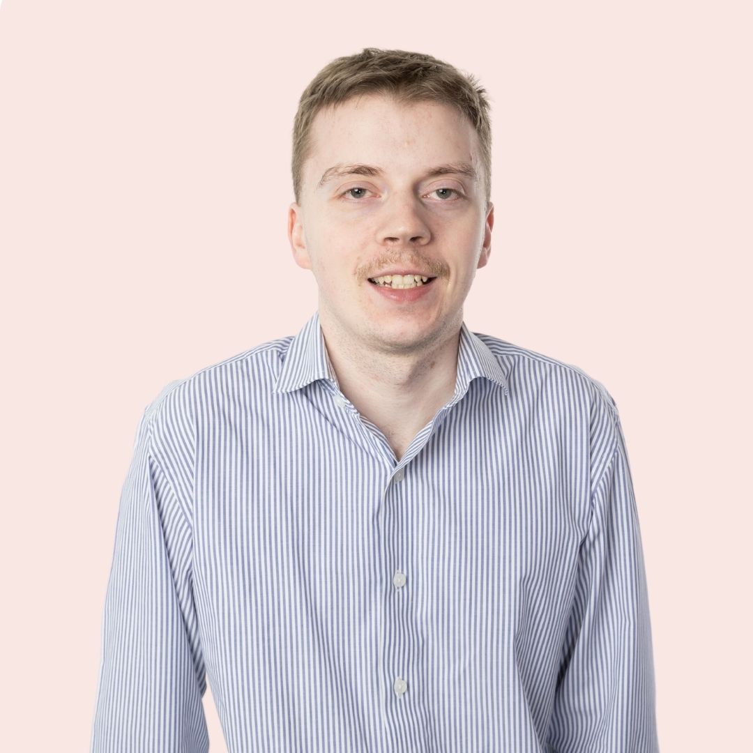 A man with short brown hair is smiling directly at the camera, he is wearing a blue and white stripe shirt